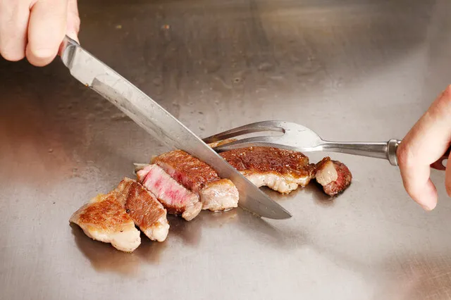 画像：鉄板の上でステーキを切っている