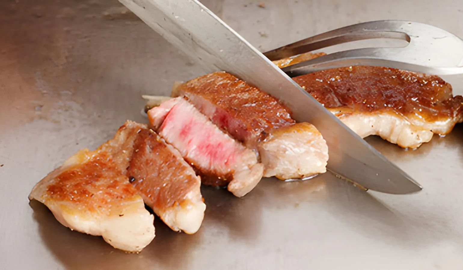 画像：鉄板の上でステーキを切っている